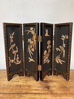 Full view of the four-panel miniature Asian style folding screen showing black lacquer background with gold-tone floral and bird motifs.