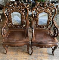 Front view of two solid wood arm chairs with carved backs featuring marble panels.