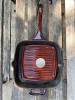 Top-down view of the brown glazed ceramic square grill pan with long handle and ribbed interior surface, showing circular Remy Olivier metal emblem at center.