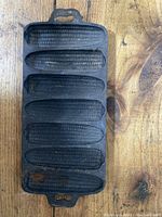 Top-down photo of vintage cast iron mold with six corncob cavities on wood surface.