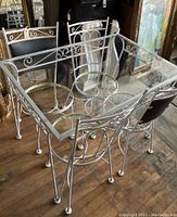 Full view of the square glass-top patio table with white wrought iron frame and four matching chairs around it, sitting on wood floor.