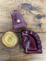 Three ceramic items shown from above on wooden surface: horse head ashtray, horse bottle, and hat ashtray.