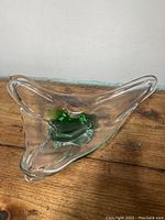 Top angle photo of a clear glass dish with green center accent, triangular shape, and smooth flowing edges on a wooden surface.