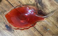 Orange art glass fish shaped dish on a wooden surface showing the overall design and color.