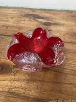 Side angled view of red and clear textured glass dish with organic wave-like edges on wooden surface