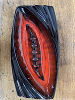 Top-down image of the ceramic ashtray showing the red/orange center with black sculpted outer frame and cigarette rests