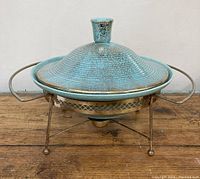 Full view of turquoise glazed pottery bowl with lid on metal stand.