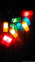 Close-up of illuminated tiki light string showing red, yellow, green, and blue tiki-shaped plastic light covers glowing.