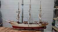 Side view of the entire wooden tall ship model showing three masts, sails rolled up, and the white and red hull mounted on a wooden base.