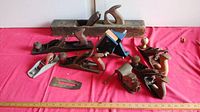 Overview of all items on red cloth including multiple wooden and metal hand planes and two small vices