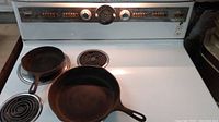 Photo of two Wagner Ware cast iron skillets on a white stove surface, showing size difference and handles.