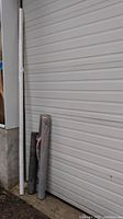Three mostly full rolls of gray air and water barrier construction material standing upright by a wall and garage door.