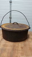 Full view of large cast iron cook pot with lid on, showing rust and wire handle
