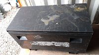 Closed black steel job box showing top surface with scratches and paint wear