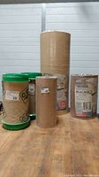 Four wood veneer rolls wrapped in brown protective paper with green plastic lids on some. Various sizes and labels visible.