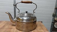 Full side view of the silver-plated antique copper kettle with wooden handle on a wooden surface.