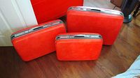 Photo showing three orange vintage Samsonite suitcases of different sizes arranged on wood floor, highlighting exterior condition and design.