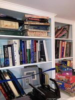 Bookshelf full of books including cookbooks on top and a stack of boxed games Yahtzee, Checkers, Backgammon