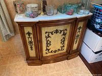 Front view of wood cabinet with stone top and decorative carved panel front.