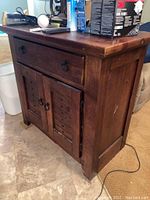 Front view of rustic wooden cabinet showing one drawer with round metal pull above two doors with matching pulls. Scratches present on front and side panels.
