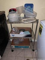 Front view of metal cart with plastic containers and lids on top shelf and boxes on lower shelves