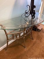 Front angled shot of demilune glass top table showing curved transparent glass and bronze/gold metal frame with scroll and rope design.