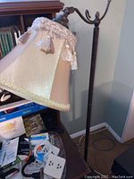 Full view showing the floor lamp's height and dark metal base with fabric lampshade featuring tassel decoration.