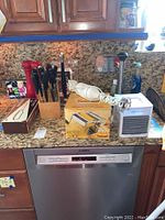 Multiple kitchen items on granite countertop including knife block, salt shakers, immersion blender, pasta maker box, and Arctic Air unit.