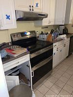 Kitchen view showing countertops with stacked plates, cutting boards, microwave, and stove with oven. Cabinets above and below counter are open with kitchenware visible inside.