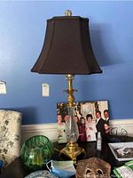 Full view of the lamp showing the pineapple metal base, clear glass body, and black fabric lampshade on a table.