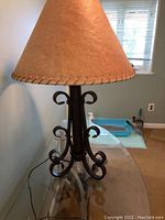 Close-up of table lamp with tan rectangular shade and ornate curled metal base