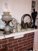 Full view of items on mantel including vintage glass lamp with etched floral shade, miniature quartz clock, two angel figurines, metal eagle bookends, large weather gauge, and black base figurine.