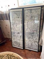 Two framed maps leaning against a wall beneath a window