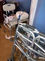 Photo showing multiple walkers including two with wheels and one without, a shower seat, assistive toilet seat, grab bar, and padded bath seat in box.