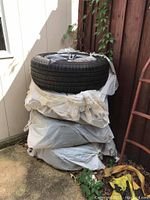 Stack of four tires wrapped in plastic at corner of yard