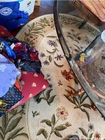 Close-up photo showing one round rug with floral pattern and braided texture under a glass table and miscellaneous items.