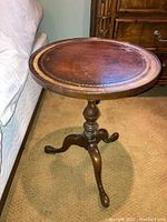 Side view of round wooden table with leather top showing pedestal base and three legs