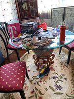 Full view of round glass tabletop supported by globe base and wooden stand in room with chairs and clutter on table.