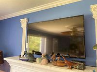 Front view of the 48 inch TV mounted on a blue wall above decorative shelf with art pieces.