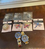 Wide view of two Invicta men's watches with blue and gold-tone bands and seven assorted pendants in original packaging on tabletop.