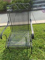 Front view of one black wrought iron rocking chair showing mesh seat, back with scrollwork, and curved armrests