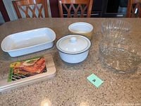Overview of all lot items on kitchen counter: white ceramic casserole, lidded pot, cream bowl, two clear glass bowls, and cedar planks