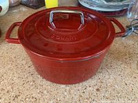 View of the closed deep red Dutch oven with metal handle and two side handles. '6 QUART' embossed on lid.