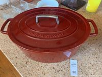 Top and side view of deep red oval Dutch oven with lid featuring embossed brand and size markings.