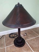 Front view of Craftsman style desk lamp with conical amber shade and dial dimmer, placed on tiled floor.
