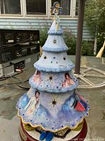 Front angle showing blue glittered porcelain Christmas tree adorned with images of Elvis Presley in white jumpsuit and light blue background, star cutouts, blue gemstones, wooden base with plaque, lightning bolt and TCB emblem on top.