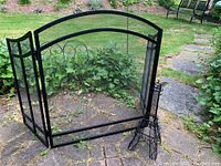 Overall view of black metal fireplace screen with mesh and Eiffel Tower statue on stone patio.
