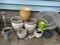 Wide view of all pots and accessories together outdoors against wall, shows variety of planters and watering can.