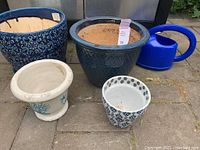Five flower pots and planters arranged outdoors, showing their textures, colors, and condition.