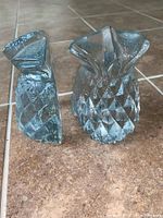 Side view of the pair of textured glass pineapple-shaped bookends on a tiled floor.